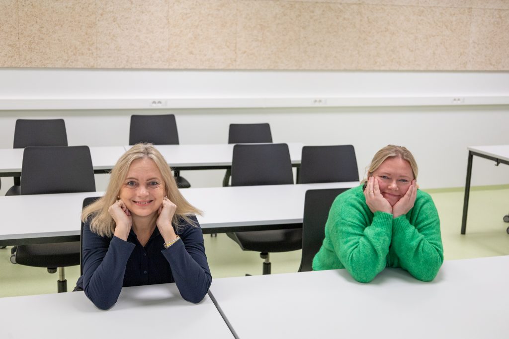 Anne Lilleaasen og Silja Bjørkly som sitter på hver sin skolepult og smiler