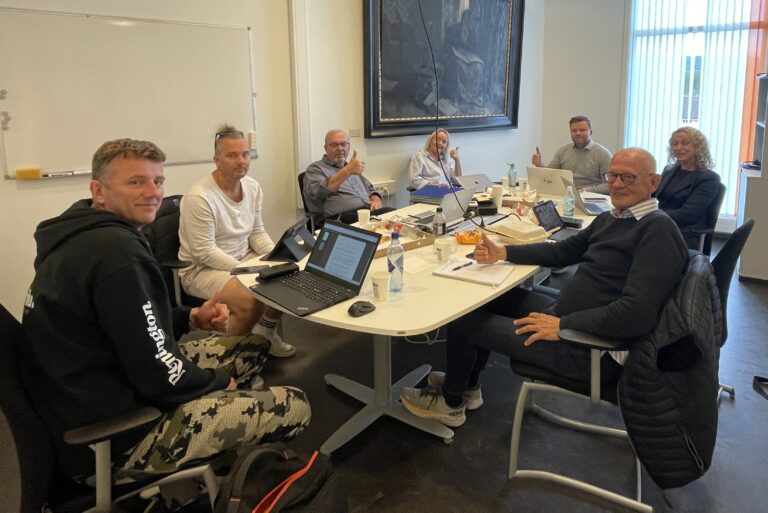 Bilde av en gruppe mennesker på et møte rundt et bord med pizza på bordet.