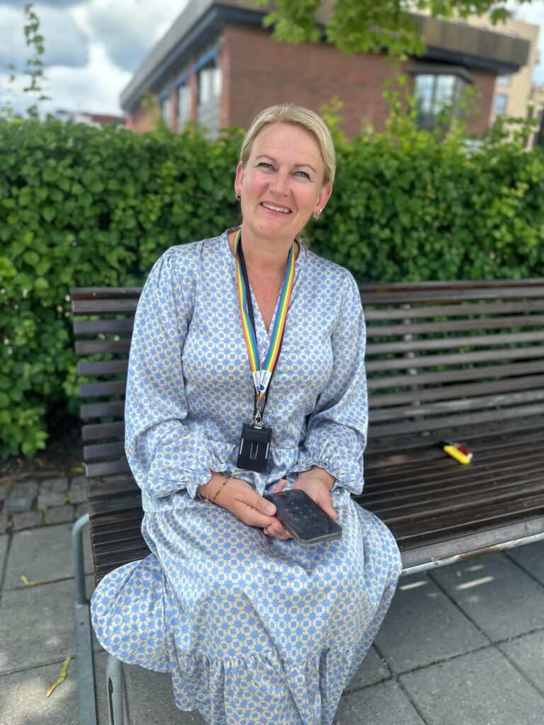 Cecilie sitter i lyseblå sommerkjole på en benk foran Nordre Follo Rådhus