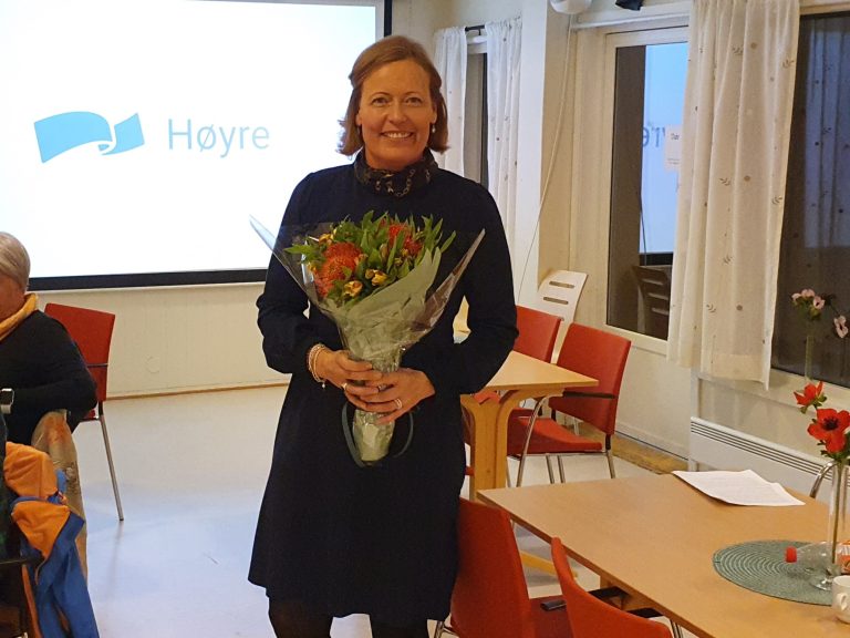 Bilde fra nominasjonsmøte. Kvinne står med en blomsterbukett i hendene, foran en Høyre-logo.