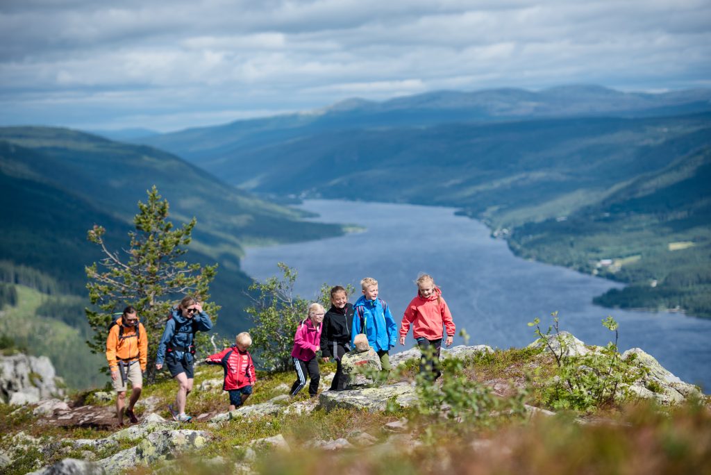 Barn på tur opp på fjellet. Dalen med en sjø i bakgrunnen. Fjell i horisonten.